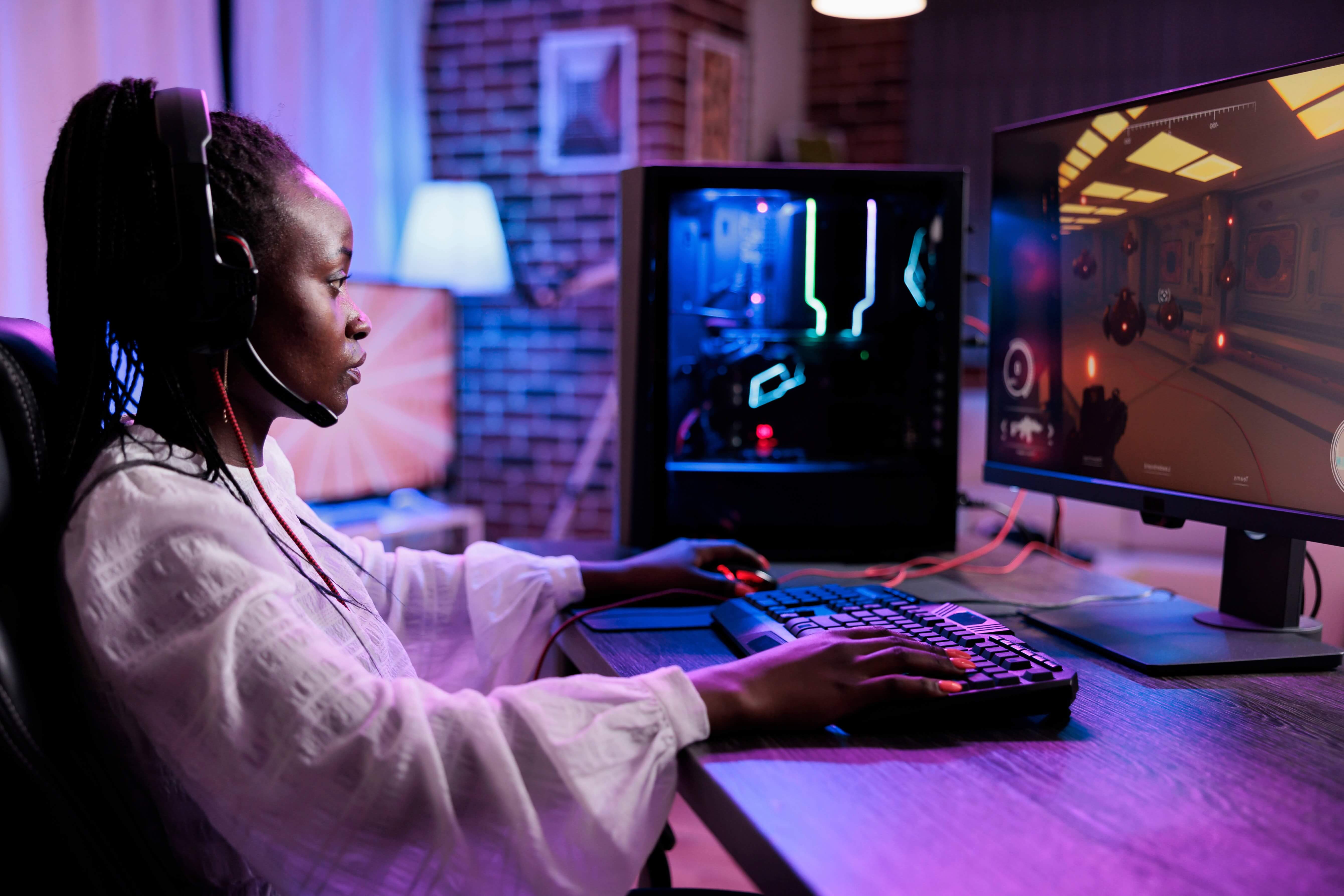 Gamer wearing headset playing online video game on dual-monitor gaming PC setup, representing high-bandwidth subscriber experience protected by cSurance network reliability